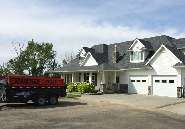 Jason's Boss Roofing trailer, phone number down the side, parked in the driveway of a finished Central Alberta job.