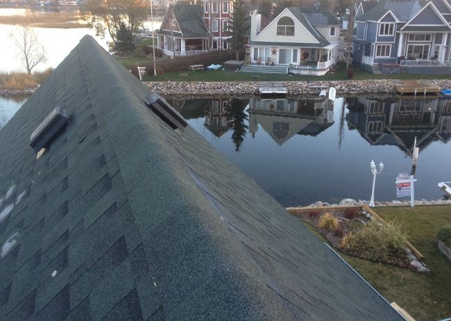 A steep shingled roof photographed from its ridge above the water at dusk.