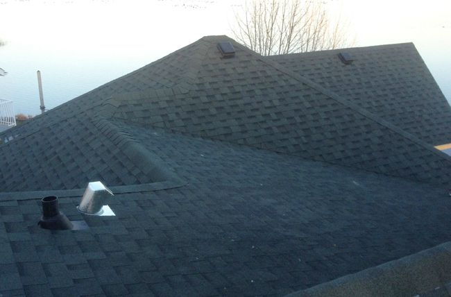The shaded plane of a Boss Roofing shingle roof at dusk, seen from the ridge above the water.
